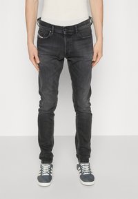 Mustad teksad, mis on slim-fit lõikega, omavad klassikalist viit taskut ja kontrastõmblusi. Komplementitud siniste sportlike jalanõudega, millel on valged triibud.