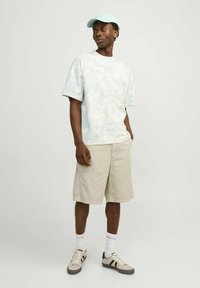 T-shirt azzurro tie-dye, pantaloni cargo beige, cappellino azzurro, calzini bianchi e sneakers grigie con strisce nere. Design casual, vestibilità rilassata.