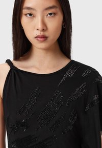 Mustat t-paidat, joissa on olkapääyksityiskohta, ja niissä on tekstuurisia helmikuviota kankaan pinnalla. Pehmeä materiaali ja sileä pinta.