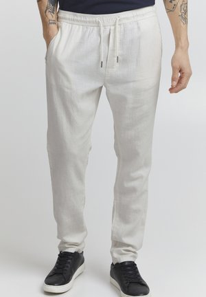Helle beige Leinen-Jogginghosen mit einem elastischen Bund, Kordelzug, Seitentaschen und schmal zulaufenden Beinen, kombiniert mit schwarzen Sneakers.