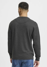 Dark gray sweatshirt with a round neckline, long sleeves, and ribbed cuffs, paired with blue denim jeans, viewed from the back.
