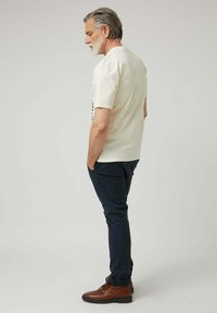 Camisa de manga corta crema con cuello redondo, combinada con pantalones navy y botas marrones de cordones, presentando un diseño simple y casual.