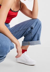 Baskets blanches, jeans bleus retroussés et débardeur rouge avec bretelles noires. La tenue présente des textures douces et décontractées ainsi que des couleurs contrastées.