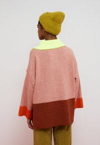 Oversized strikket sweater i pink, brun og orange med en lys grøn krave. Har en kasseformet pasform og løstsiddende ærmer.