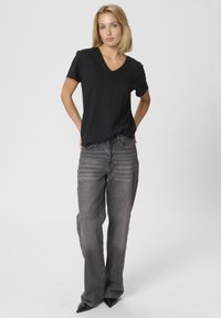 Čierne V-krčný tričko v kombinácii s rovnými sivými džínsami. Džínsové nohavice majú jemné horizontálne pruhy. Celkový vzhľad dopĺňajú čierne lodičky s ostrou špičkou.