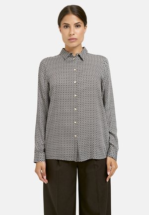 Button-up shirt in black and white geometric pattern, featuring a collar, long sleeves, and golden buttons. Smooth fabric with slight sheen.