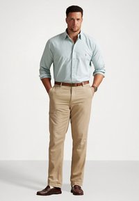 Ανοιχτό μπλε πουκάμισο με κουμπιά, μπεζ chino παντελόνι, καφέ ζώνη και καφέ παπούτσια. Το πουκάμισο έχει ένα μικρό λογότυπο στο στήθος.