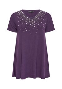 Violetti lyhythihainen tunika V-pääntiellä, jossa tähtimuotoisia koristeluita kultaisina ja hopeisina, laskeutuva leikkaus ja pehmeä kangas.