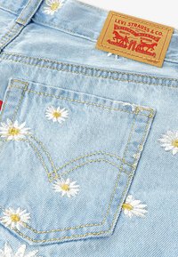 Υφασμα από ανοιχτό μπλε τζιν με κεντημένα λευκά μαργαριτάρια με κίτρ ινα κέντρα και χρυστή ραφή. Η ετικέτα γράφει "Levi Strauss & Co."