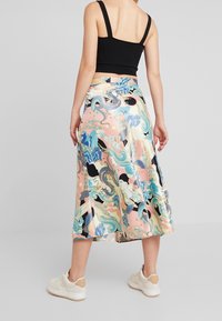 Jupe midi fluide dans des couleurs pastel avec des motifs complexes de dragons et de vagues. Elle présente une taille ajustée et un détail d'ouverture, associée à des baskets blanches.