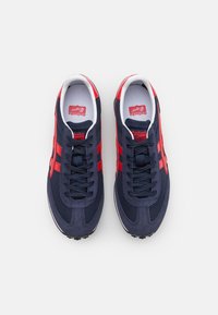 Sneaker blu navy con strisce rosse, materiali in rete e camoscio, punta tonda, suola piatta e colletto imbottito. Logo rosso sulla linguetta.