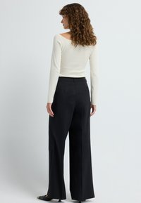 Langermige, off-white top met een rechte halslijn, gecombineerd met hooggepollode, wijde zwarte broeken. Getextureerde stof en op maat gemaakte uitstraling.