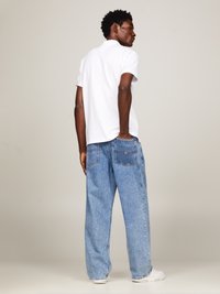 Camisa polo blanca y vaqueros de mezclilla blue claros y holgados. Los vaqueros tienen detalles en las costuras y dos bolsillos traseros. Combinado con zapatillas blancas.