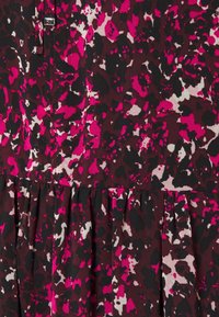 Le tissu de la robe multicolore présente une base brun foncé avec des motifs abstraits vibrants en rose et blanc, texturé par des plis froncés au niveau de l'ourlet.