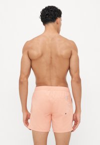 Shorts de bain pêche en tissu léger, dotés d'une taille élastique, de poches latérales et d'une poche arrière avec un bouton.