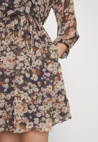 Kukkamekko kevyestä, läpikuultavasta kankaasta, jossa tummantaustalla on vaaleanpunaisia, valkoisia ja oransseja kukkia, vyötärösolki ja pitkät hihat.