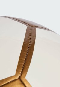 Valkoinen jalkapallo, jossa on kiiltävä pinta ja ruskea tikattu sauma geometrisella kuviolla, korostaen sen tekstuuripintaa.