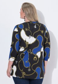 Svart topp med mönster av kedjor och accessoarer i guld, blått och vitt, med trekvartslånga ärmar och avslappnad passform.