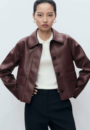 Bordeaux faux leren cropped jack met een kraag, knoopsluiting, twee voorkanten zakken en een soepele textuur, gedragen over een witte polo.