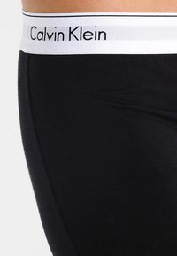 Melnas kokvilnas jostas daļa ar "Calvin Klein" logo baltā krāsā, ar gludu tekstūru un diskrētām plakanām šuvēm komfortam.