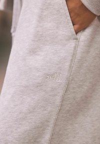 Hellgrau sweatshirt mit weichem Material, seitlicher Tasche und gesticktem "self."-Detail am unteren Saum.