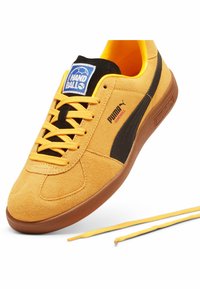 Gele suède handbalsneakers met zwarte accenten en rubberen zolen. Voorzien van ronde veters en een blauwe label op de tong.