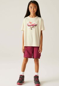 Camiseta de color crema claro con un gráfico de corazón colorido. Pantalones cortos burdeos oscuros. Zapatillas deportivas grises y rosas con calcetines blancos. Un atuendo simple y casual.
