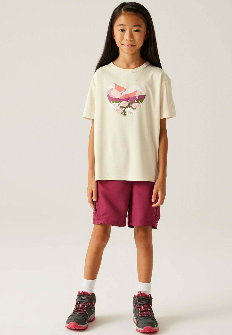 Camiseta de color crema claro con un gráfico de corazón colorido. Pantalones cortos burdeos oscuros. Zapatillas deportivas grises y rosas con calcetines blancos. Un atuendo simple y casual.