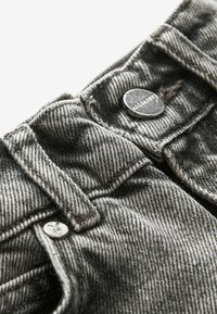 Vaqueros de denim gris con una superficie texturizada, que presentan botones de metal plateado y detalles de costura en contraste en la cintura y los bolsillos.