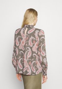 Blouse à motifs marron avec des designs paisley et à pois. Présente des manches longues et un détail dos en forme de trou de serrure. Texture de tissu lisse.