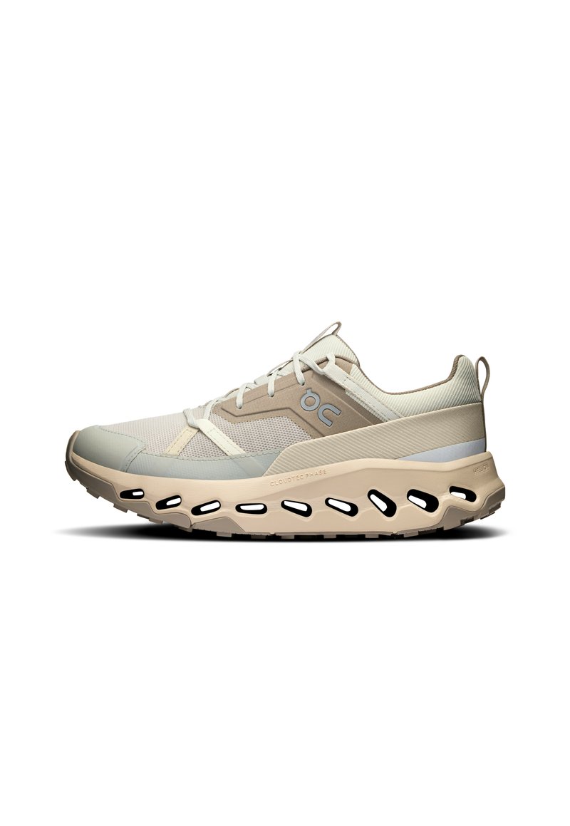 Beige Laufschuh mit einem Netzoberteil, hellgrauen Akzenten und einer wolkenartigen Sohle mit Ausschnitten für Atmungsaktivität und Flexibilität.