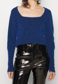 Blå, texturerad stickad tröja med fyrkantig halsringning och långa ärmar, kombinerad med högmidjade, glänsande svarta läderbyxor.