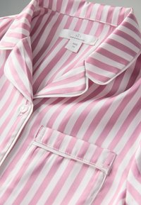 Rózsaszín és fehér csíkos pizsamaing, kivágott nyakkal, egy mellzsebbel, sima szatén anyagból, gombos záródással. A címke szerint 7 éves méret.