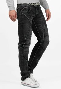 Zwarte denim jeans met contrasterende witte stiksels, slim fit, meerdere zakken inclusief een met rits, gecombineerd met witte sneakers.