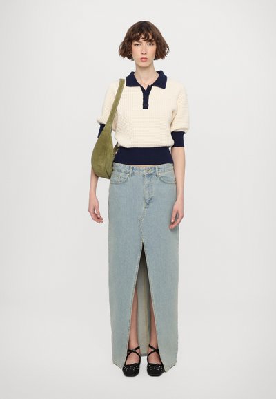 Pull en maille crème avec des accents bleu marine, associé à une jupe maxi en denim clair avec une fente à l'avant. Chaussures noires avec un détail en nœud.