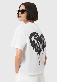 Hvid kortærmet T-shirt med et stort sort dryppende hjertegrafik på ryggen. Designet har en afslappet pasform og blød tekstur.