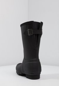 Botas de lluvia de goma negra con acabado texturizado, detalle de hebilla lateral y suela con relieve. Diseñadas para ser duraderas y ofrecer un rendimiento impermeable.