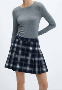 Un haut gris à manches longues associé à une jupe plissée à carreaux marine, arborant des lignes blanches et marron clair dans un motif à carreaux classique.
