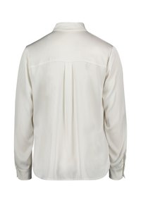 Langärmlige cremefarbene Bluse mit glatter Textur, Kragen und einem mittigen Rückenschlitz. Die Manschetten haben Knopfakzente zur Befestigung.
