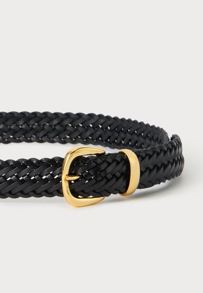 Ceinture en cuir tressé noir avec une petite boucle en métal doré et une boucle sur un fond gris clair.