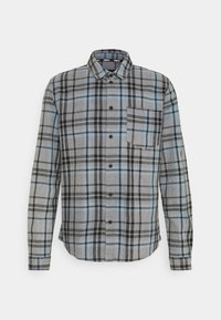 Chemise grise à manches longues avec motif à carreaux noir et bleu, boutonnage sur le devant et poche poitrine sur un fond uni.
