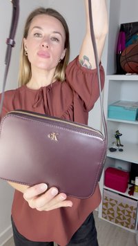 Burgundy leather crossbody bag with a zip closure and embossed logo; medium size, rectangular shape with a smooth texture.