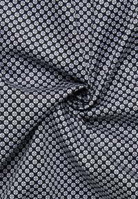 Tessuto nero con un motivo geometrico ripetitivo di piccole forme bianche e azzurre, che mostra una superficie liscia e una caduta leggera.