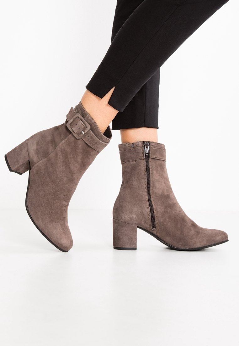 Bottines en suède taupe avec un talon épais, équipées d'une fermeture éclair sur le côté et d'une sangle décorative à boucle autour de la cheville.