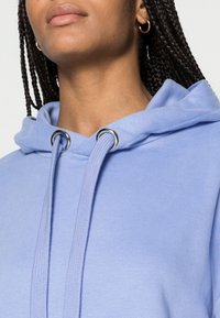 Felpa leggera blu con cappuccio e lacci, dotata di occhielli in argento. Tessuto morbido con una superficie liscia e design del cappuccio piegato.
