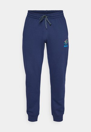 Tamsiai mėlynos sportinės kelnės, pagamintos iš švelnaus medvilninių audinių mišinio, su elastingu liemeniu ir raišteliais, bei sutrauktomis rankovėmis. Lotto logotipas kairėje pusėje.