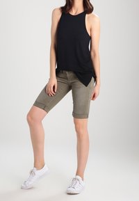 Top sin mangas negro combinado con pantalones cortos de hasta la rodilla en verde oliva. Calzado: zapatillas blancas. Diseño simple con dobladillo enrollado en los pantalones cortos.