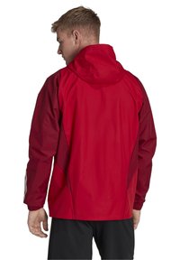 Rode, waterdichte jas met capuchon, lange mouwen en elastische manchetten. Bevat gekleurde accenten en een gladde, glanzende textuur.