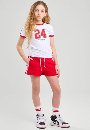 White short-sleeve t-shirt with red trim and "24" print. Red shorts with side pockets. White and black high-top sneakers. Red and white striped socks.