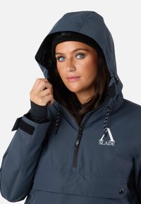 Mörkblå vattentät pulloverjacka med huva, som har en framficka, logotyp och justerbara snoddar; inkluderar svarta ärmslut.